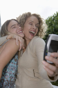Mother hugging daughter (13-15) while taking picture with mobile phone