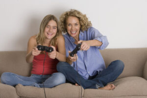 Mother and daughter (13-15) playing computer game on sofa, smiling